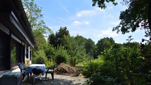 A stone-paved patio with a table and chairs, surrounded by lush greenery and trees. - Romantic Mansion in Strotzbusch by the Forest (Strotzbusch)