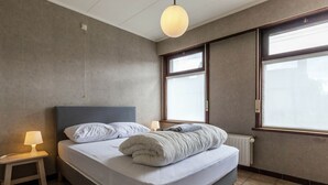 Ett sovrum med en säng, sänglampor, ett fönster och ett element.