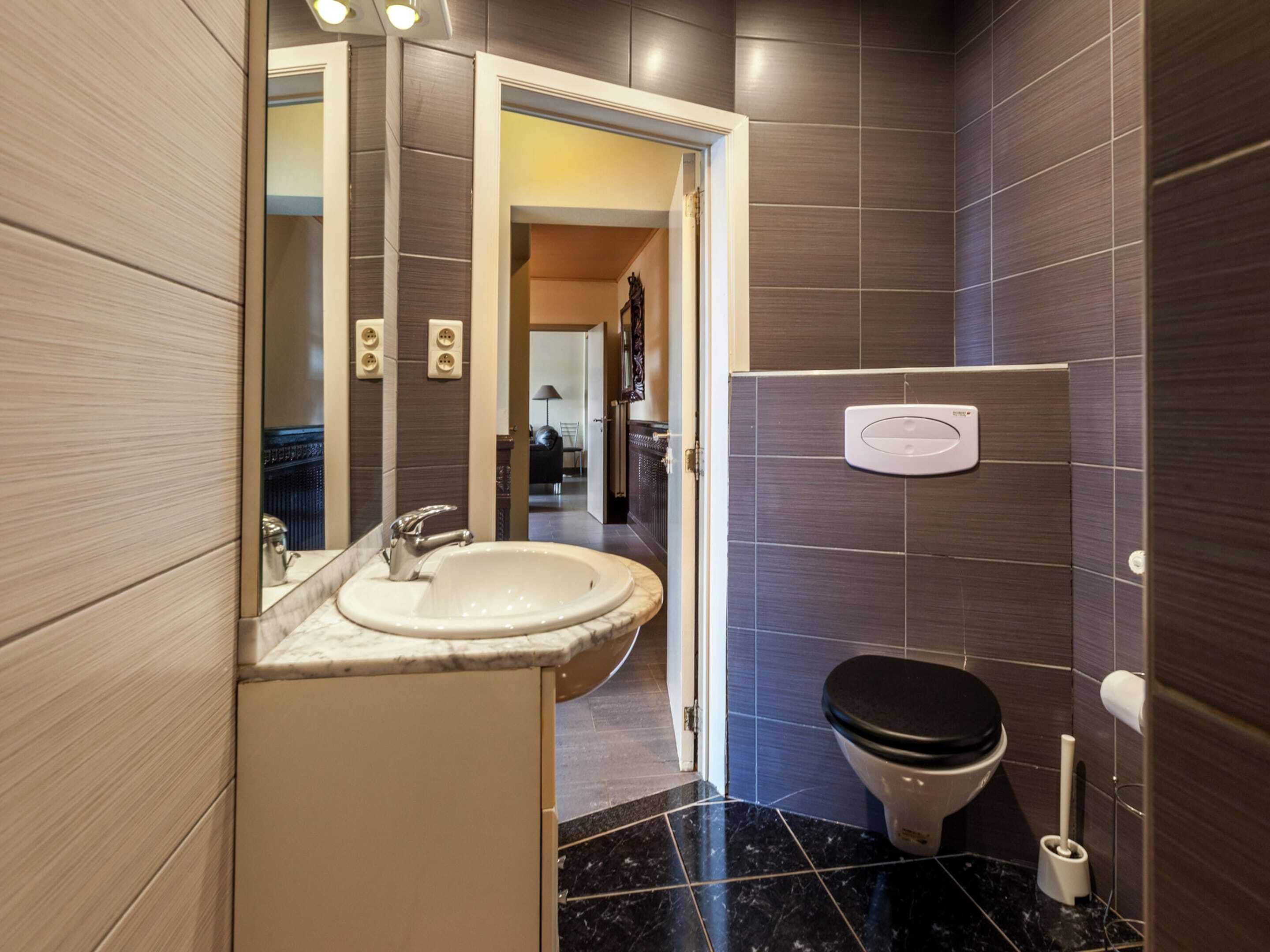 A modern bathroom with a marble sink, a toilet, and a mirror.