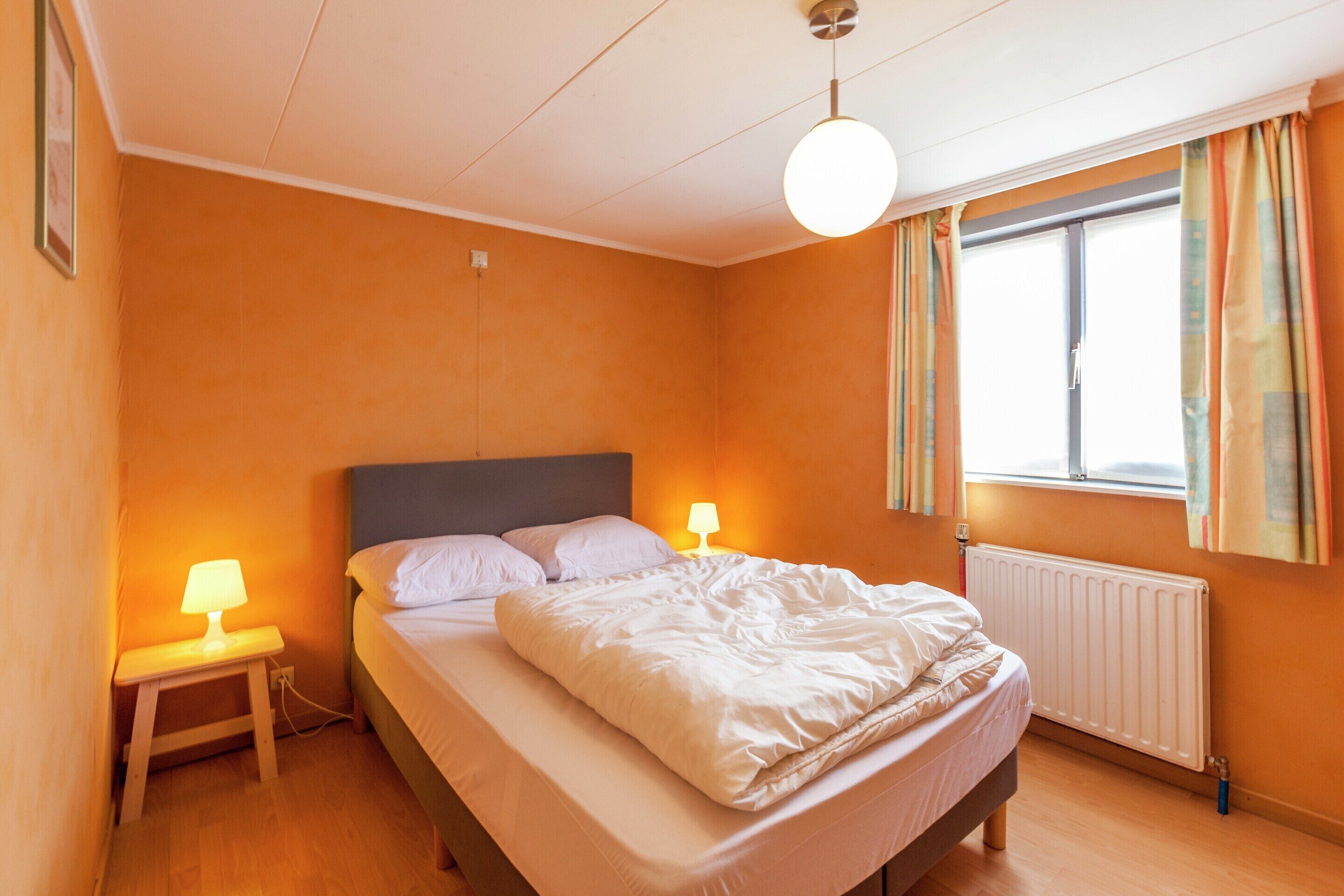 Une chambre à coucher avec un lit, des lampes de chevet, une fenêtre avec des rideaux et un radiateur.