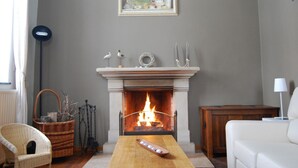 A living room with a fireplace, a framed picture above it, and a wicker chair. - Stone-built Holiday Home in Dinant With Terrace (Dinant)