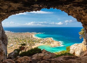 Eine Küstenstadt, die durch eine Felsspalte sichtbar ist, mit Strand, klarem blauen Wasser und weiter Meerblick.
