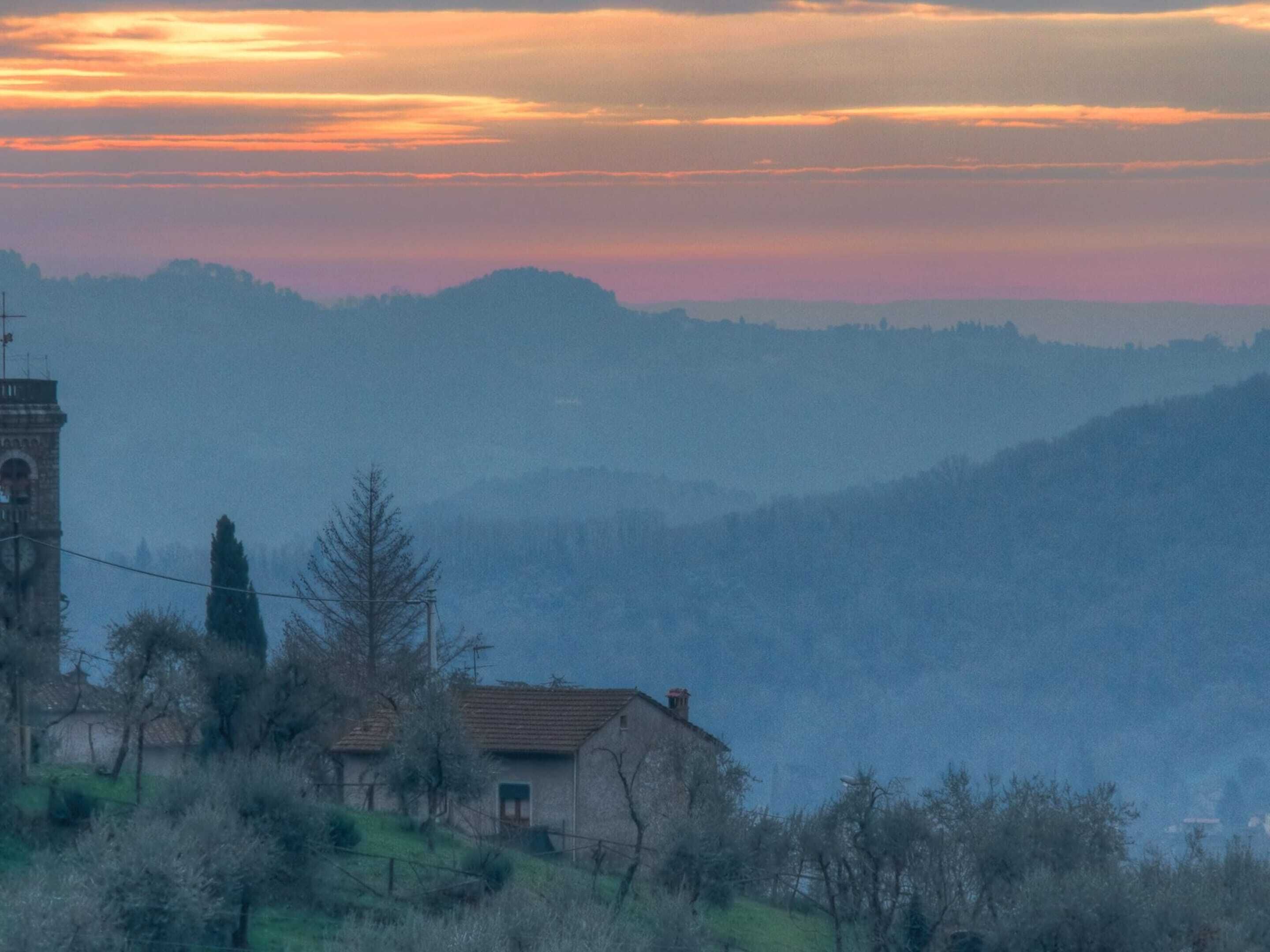 A rural landscape with a church tower, a small house, and rolling hills in the background.