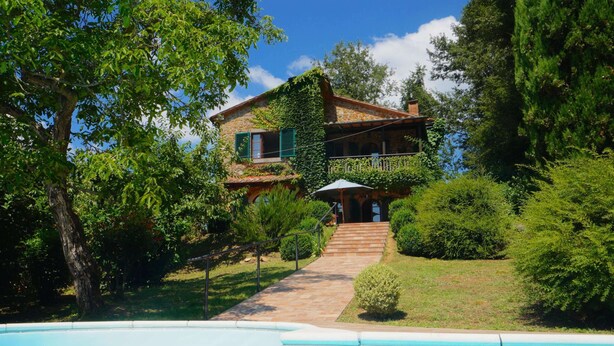 Una casa de dos pisos amb façana de pedra, piscina i jardí ben cuidat.