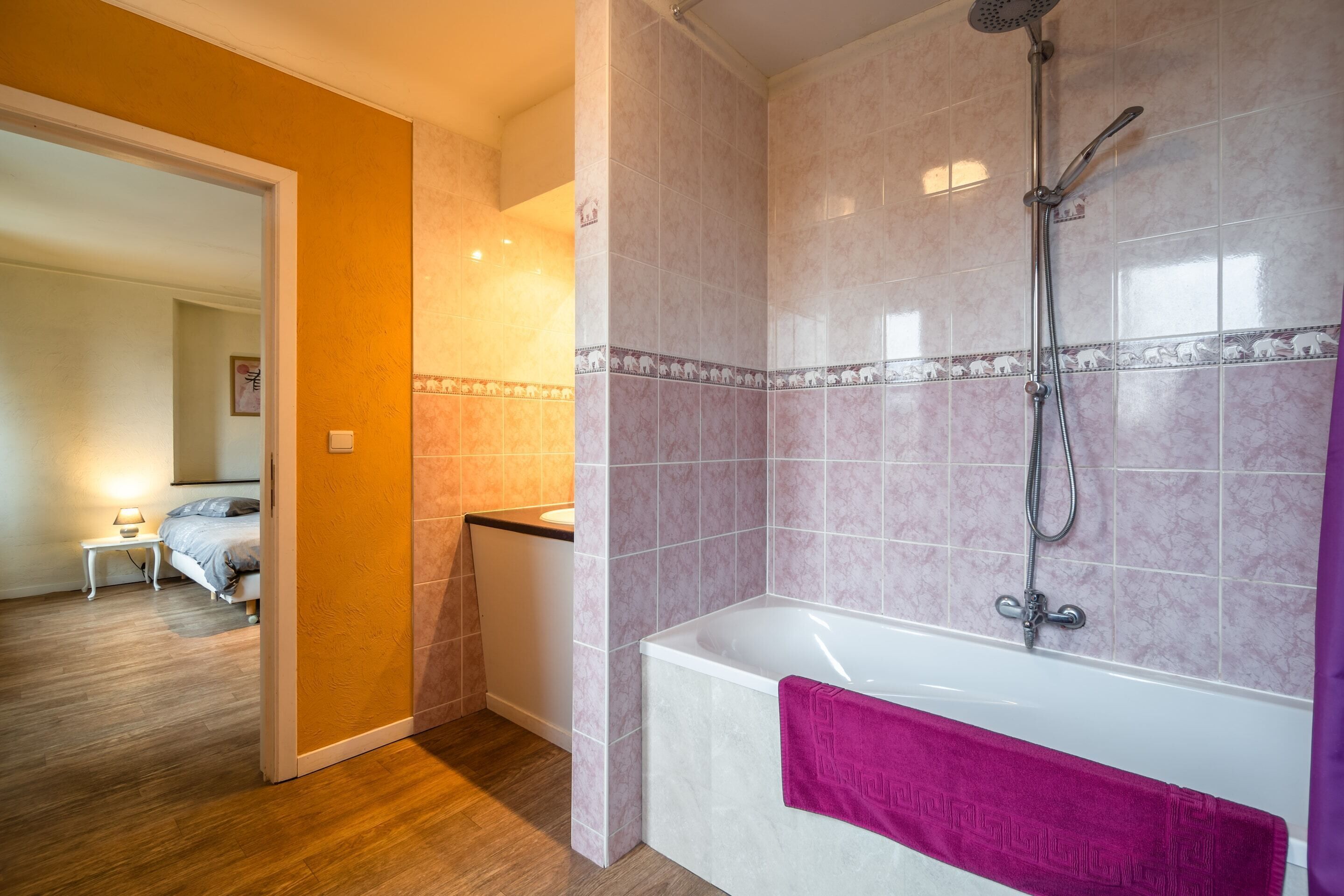 A modern bathroom with a bathtub, shower, and a wooden floor.