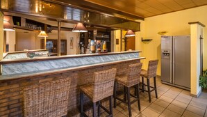 Una zona de bar con mostrador de mármol, taburetes de mimbre, un refrigerador de acero inoxidable y suelo de baldosas.
