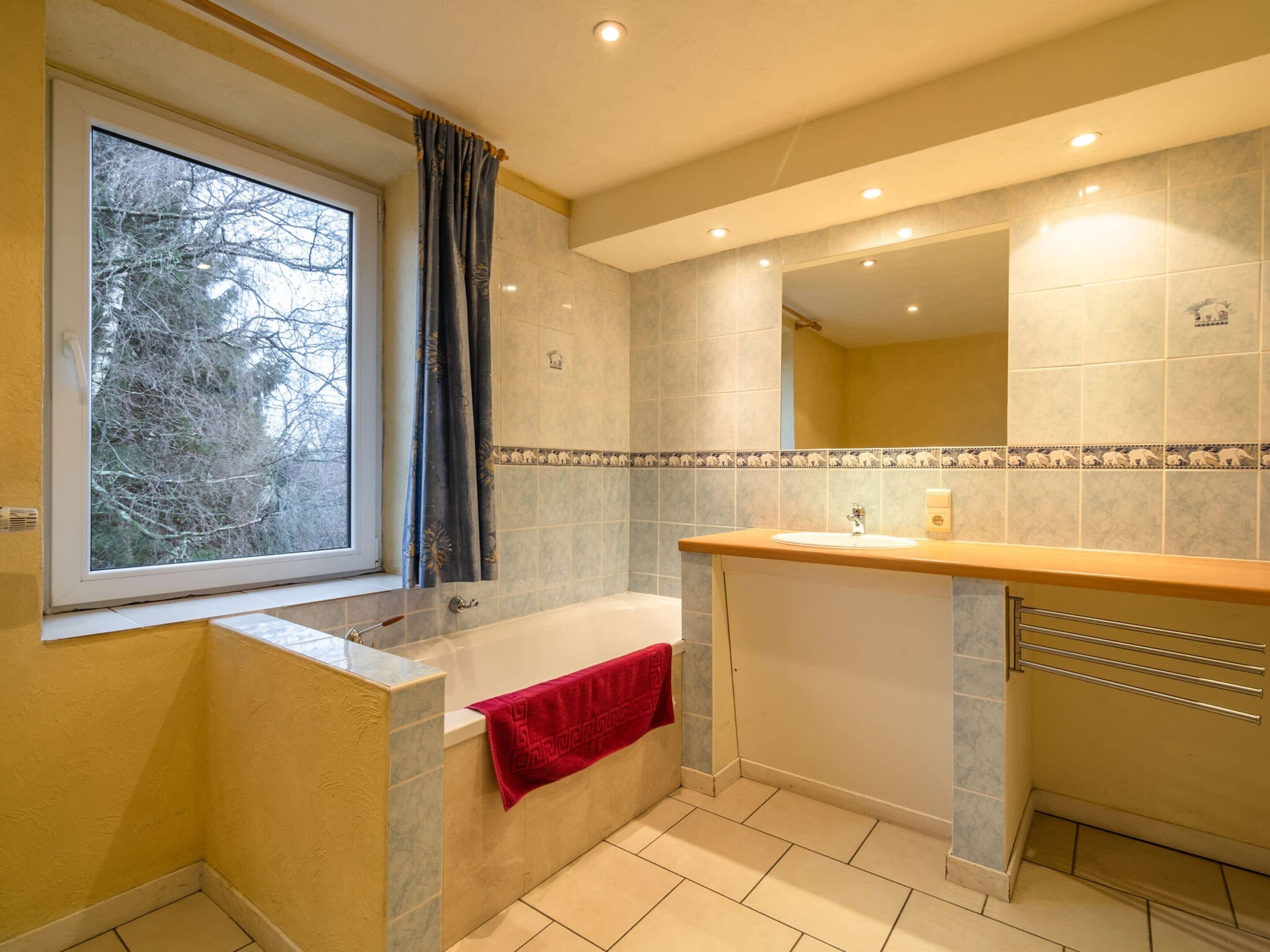 A bathroom with a bathtub, a window with curtains, a sink, and a mirror.