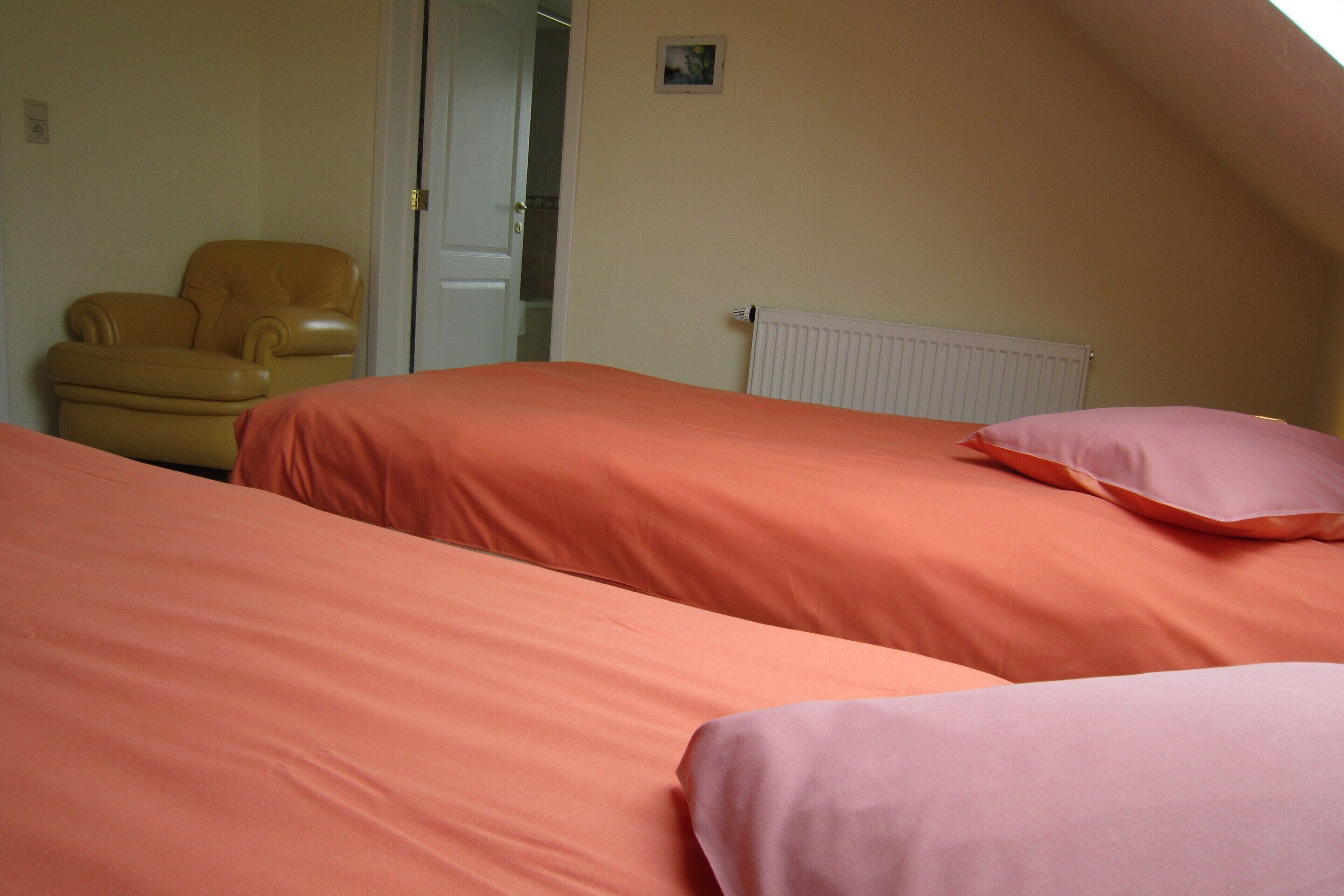 A bedroom with two beds, a chair, and a radiator.