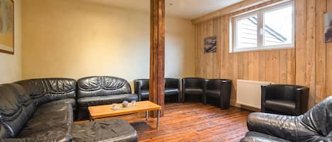Ein Zimmer mit Holzboden, einer schwarzen Ledersofa, einem Holztisch und einem Fenster mit holzverkleideten Wänden.