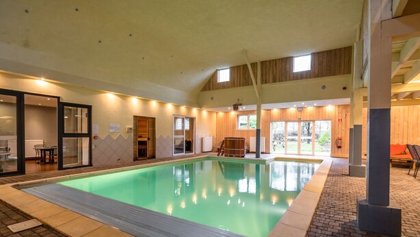 Una piscina interior con suelo de baldosas, paredes de madera e iluminación empotrada en el techo.