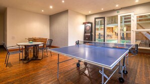 Una mesa de ping pong en una habitación con piso de madera, un dardo y vistas a una piscina exterior a través de puertas de vidrio.