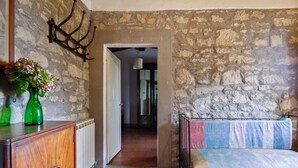 A room with a stone wall, a wooden cabinet, a green vase with flowers, a bed with a colorful blanket, and a door leading to another room. - Hillside Retreat With a View (Castelfranco Piandisco)