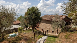 A rustic stone building with a tiled roof, a stone pathway leading to a wooden bench, and a clear view of the surrounding landscape. - Hillside Retreat With a View (Castelfranco Piandisco)