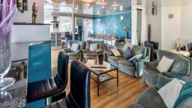 Um amplo hall de hotel com design moderno, apresentando sofás de couro, uma mesa de centro e uma grande parede azul.