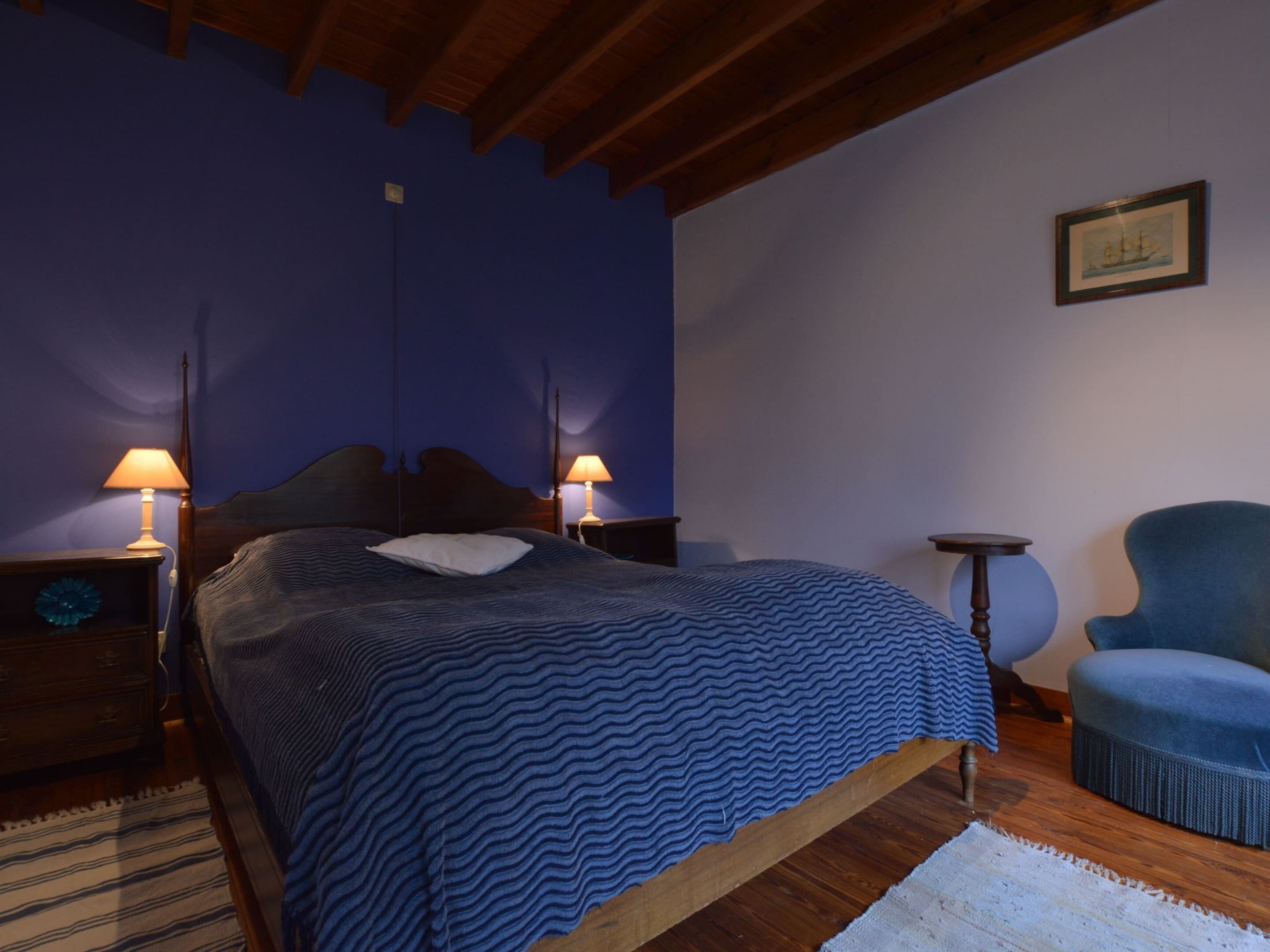 Une chambre à coucher avec un lit, deux tables de chevet avec des lampes, une chaise et un tableau encadré au mur.