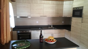 Une cuisine moderne avec des meubles de couleur bois clair, un plan de travail noir, un four encastré et un four à micro-ondes.