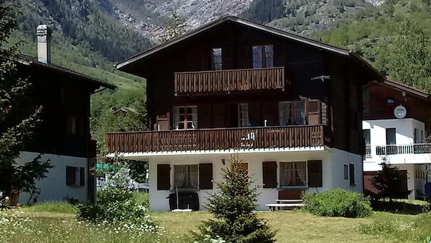 Un bâtiment de style chalet doté d’un balcon, entouré d’un paysage montagneux.