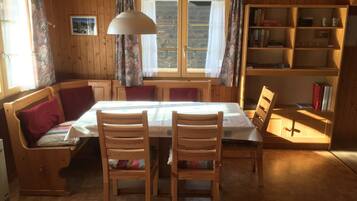 A cozy room with a wooden interior, a dining table with chairs, a bookshelf, and a window with curtains.
