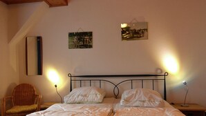 Un dormitorio con una cama, dos mesitas de noche, una silla y dos cuadros en la pared.