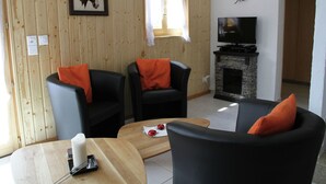 Un salon avec deux fauteuils noirs, une table basse en bois, une cheminée et un téléviseur posé sur une étagère en pierre.