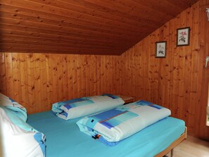 A wooden-paneled room with two beds, each with blue bedding and pillows.