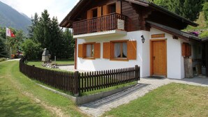 Un chalet en bois à deux étages, doté d’un balcon, d’une clôture en bois et surplombant un paysage montagneux.
