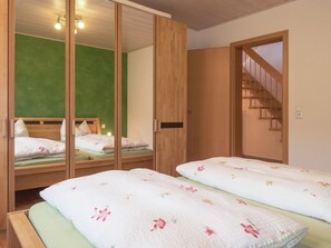 A room with two beds, a green wall, wooden furniture, and a staircase.