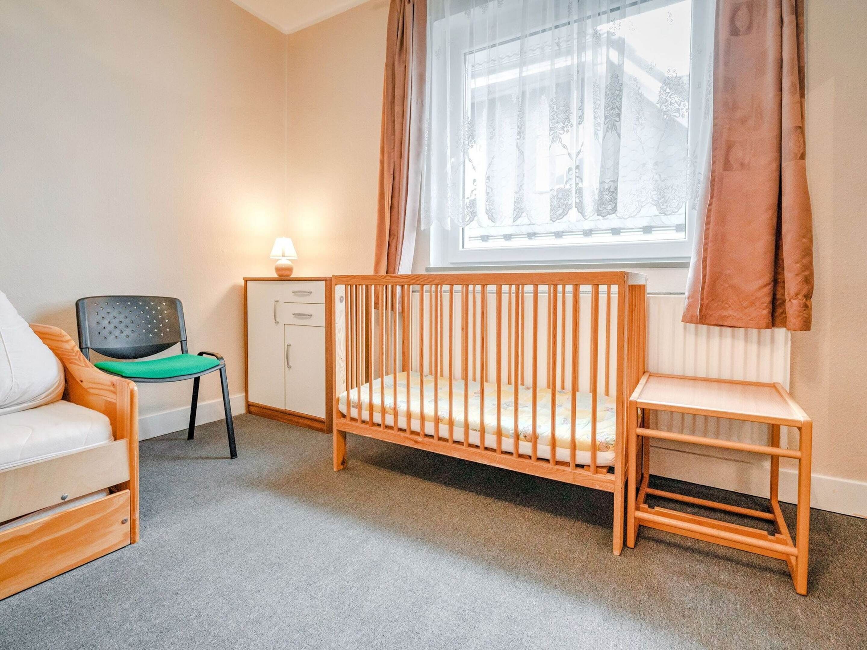 Ein Babyzimmer mit einem Kinderbett, Wickeltisch, Stuhl, Schrank und einem Fenster mit Vorhängen.