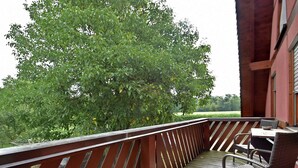 Una terraza de madera con una mesa y sillas, con vistas a un paisaje verde y un árbol.