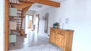 Un pasillo espacioso con una escalera de madera, suelo de baldosas y un armario de madera con botellas.