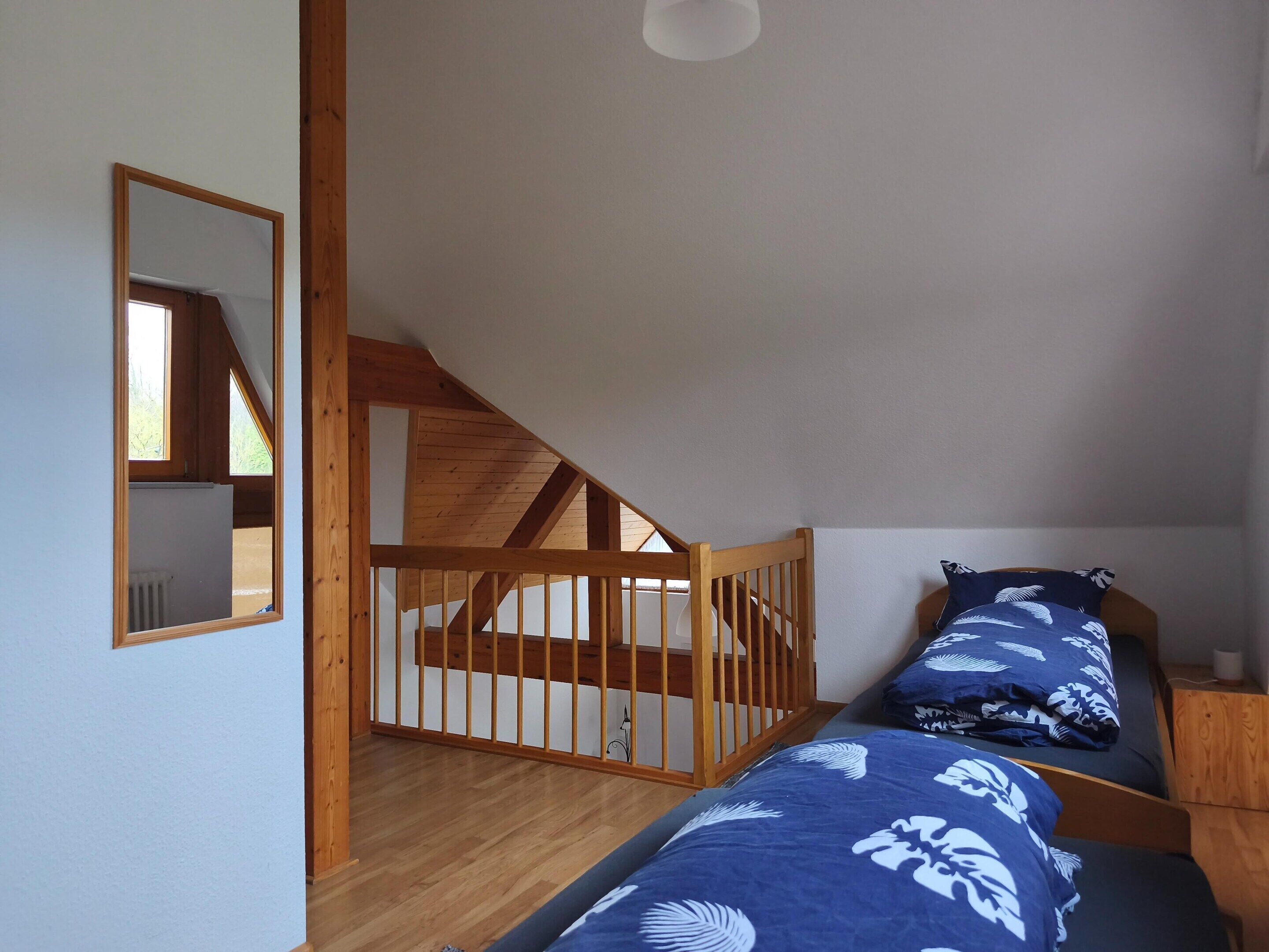 Un dormitorio con escalera de madera, dos camas con ropa de cama azul estampada con flores, cabeceros de madera y un espejo en la pared.