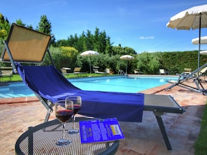 A poolside area with a lounge chair, a table with a glass of red wine, and a menu.