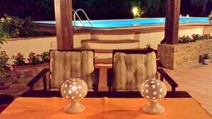 An outdoor seating area with two chairs and two decorative globes on a woven mat, overlooking a pool. - Belvilla by OYO Villa in Caltagirone (Caltagirone)