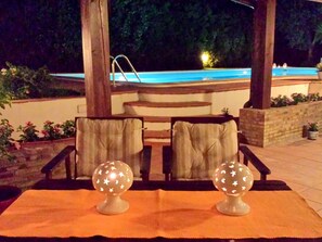 An outdoor seating area with two chairs and two decorative globes on a woven mat, overlooking a pool. - Belvilla by OYO Villa in Caltagirone (Caltagirone)