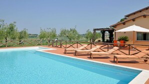 Une piscine dotée de chaises longues et d’une pergola, entourée d’une clôture en bois et de verdure.