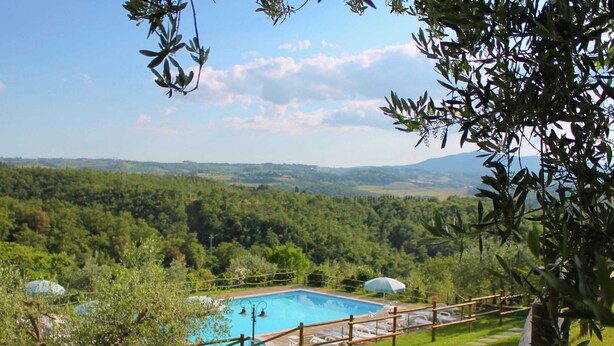 A pool with a wooden deck and lounge chairs, surrounded by lush greenery and a view of distant hills. - Scenic Farmhouse With Pool (Citta della Pieve)