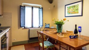 A dining area with a wooden table, chairs, a vase with flowers, a bottle of wine, and a painting on the wall. - Belvilla by OYO Vintage Holiday Home in Montaione (Montaione)