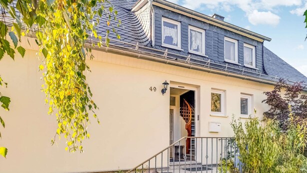 Een tweelaags huis met een grijs dak, een beige gevel en een zichtbare trap naar de ingang.