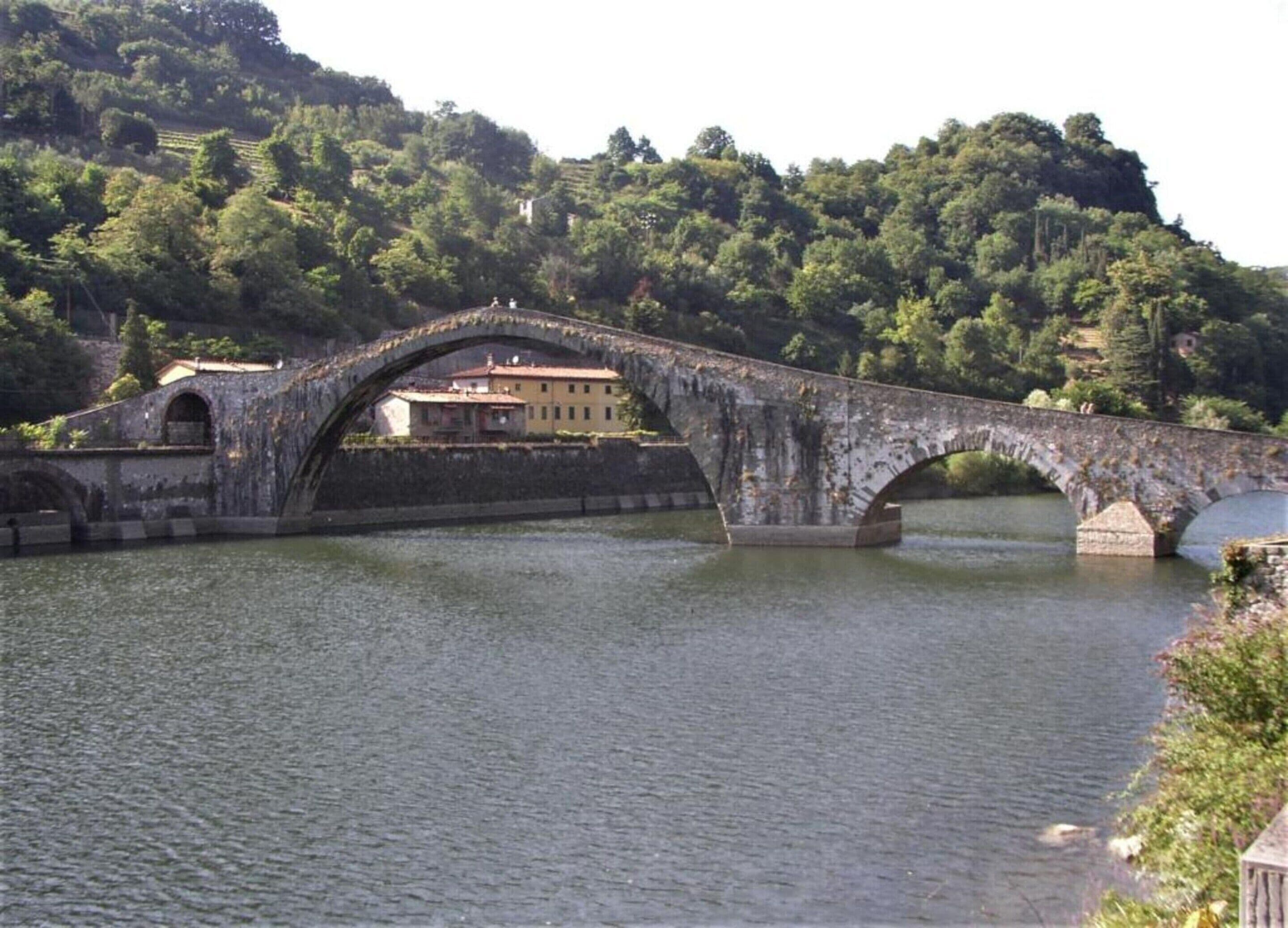 Eine Stebrücke über einem Fluss, im Hintergrund ein Gebäude.