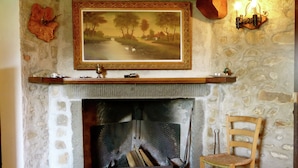 A stone fireplace with a framed painting above it, a wooden chair to the right, and a wall-mounted light fixture. - Cottage in Casoli Near Ski Slopes (Bagni di Lucca)