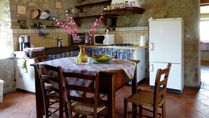 A rustic kitchen with a stone wall, wooden ceiling, and a dining table with chairs. - Cottage in Casoli Near Ski Slopes (Bagni di Lucca)