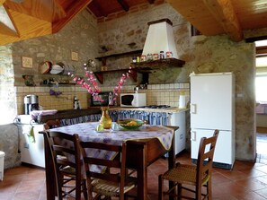 A rustic kitchen with a stone wall, wooden ceiling, and a dining table with chairs. - Cottage in Casoli Near Ski Slopes (Bagni di Lucca)