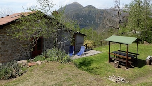 A stone building with a small porch, a wooden bench, and a green shelter. - Cottage in Casoli Near Ski Slopes (Bagni di Lucca)