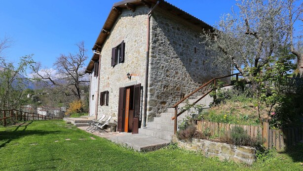 A stone building with a wooden door and windows, a grassy yard, and a staircase leading up to the entrance. - Cottage in Casoli Near Ski Slopes (Bagni di Lucca)