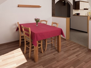 A dining area with a table set for four, wooden chairs, a vase with flowers, and a wooden shelf above the table.