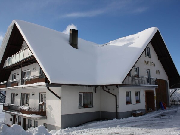 A two-story building with a steeply pitched roof covered in snow, a balcony on the second floor, and a sign reading "MATTEN HOF".