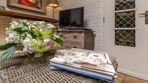 A wicker table with a magazine, a vase of flowers, and a television on a wooden cabinet against a white brick wall. - House in Zingem Near Hiking Trails (Kruishoutem)