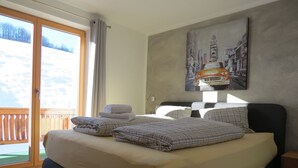 Een slaapkamer met een bed, kussens, een schilderij en uitzicht op een besneeuwd landschap door een schuifdeur.