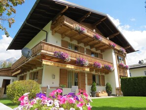 A two-story chalet with wooden balconies adorned with flower boxes, a satellite dish, and a well-maintained lawn. - Voluminous Apartment near Ski Slopes in Maria Alm (Maria Alm am Steinernen Meer)