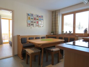 A dining area with a wooden table and benches, a wall with framed pictures, and a window with a view of trees. - Voluminous Apartment near Ski Slopes in Maria Alm (Maria Alm am Steinernen Meer)